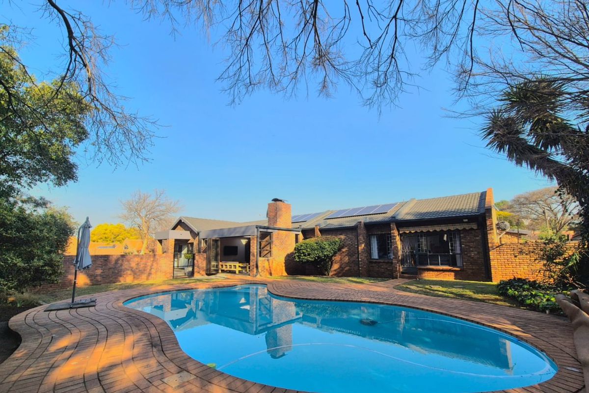 Rear view of the property featuring a swimming pool, brick paved surround, covered patio area, and solar panels installed on the tiled roof.
