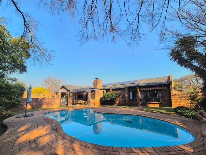 Rear view of the property featuring a swimming pool, brick paved surround, covered patio area, and solar panels installed on the tiled roof.