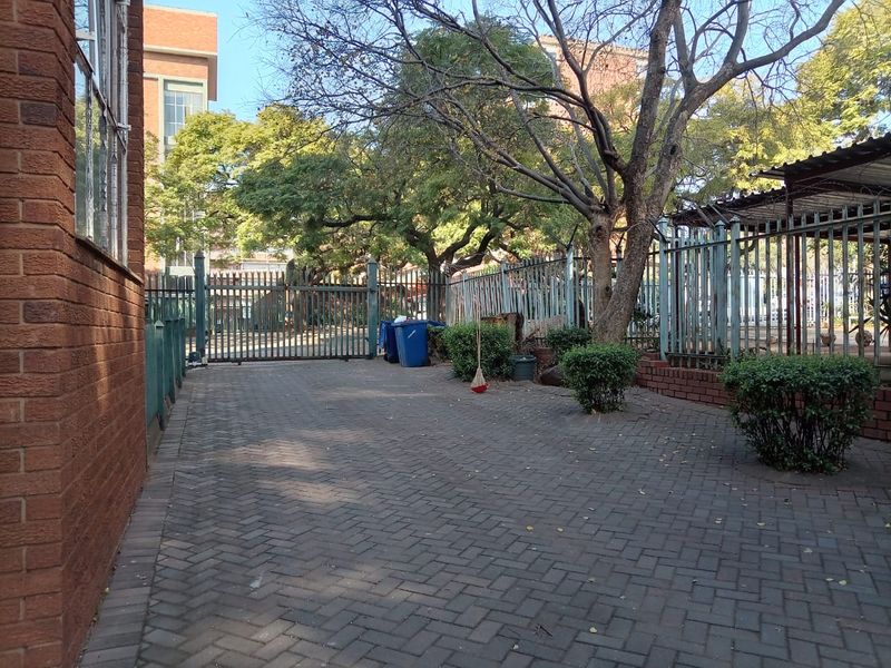A paved rear courtyard area featuring established trees, brick retaining walls, and secure metal perimeter fencing.