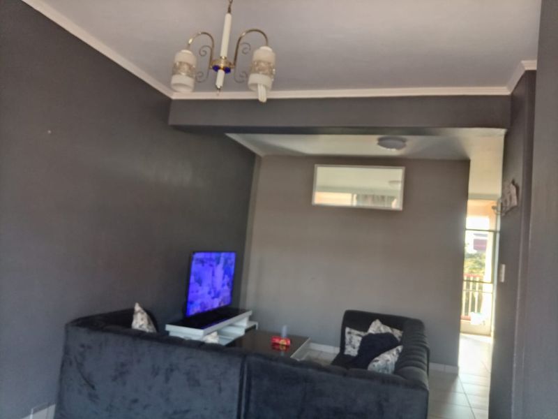 A living room area featuring dark grey walls, tiled flooring, and a recessed bulkhead ceiling detail, leading towards an adjacent balcony area.