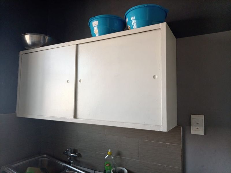 A kitchen area featuring wall-mounted cabinetry, a stainless steel sink with faucet, and a tiled backsplash.