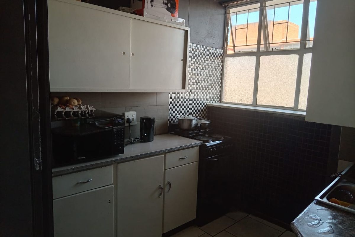 A compact kitchen featuring built-in cabinetry, tiled backsplash, and a metal-framed window, offering a functional space in need of cosmetic updates.