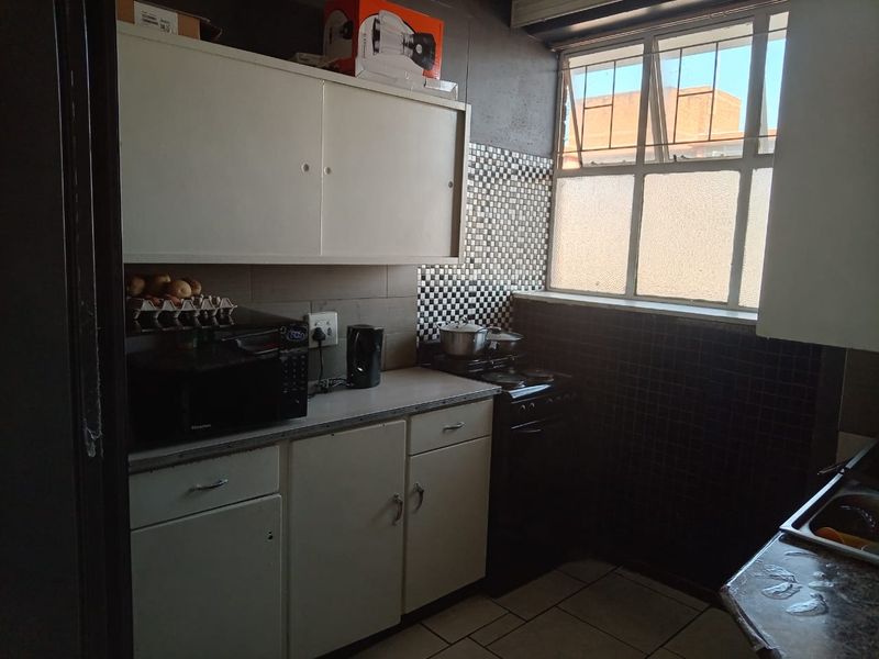 A compact kitchen featuring built-in cabinetry, tiled backsplash, and a metal-framed window, offering a functional space in need of cosmetic updates.