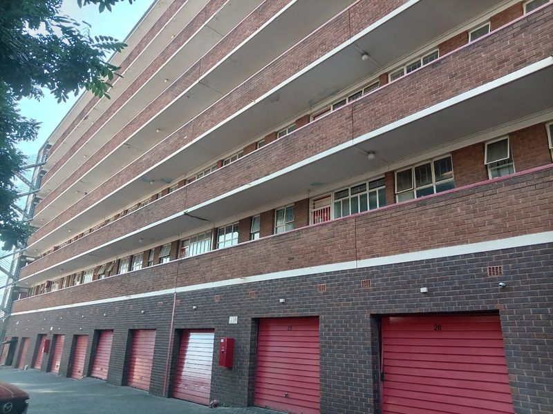Exterior view of a multi-story apartment building featuring a brick facade, multiple balconies, and ground-level garage access.