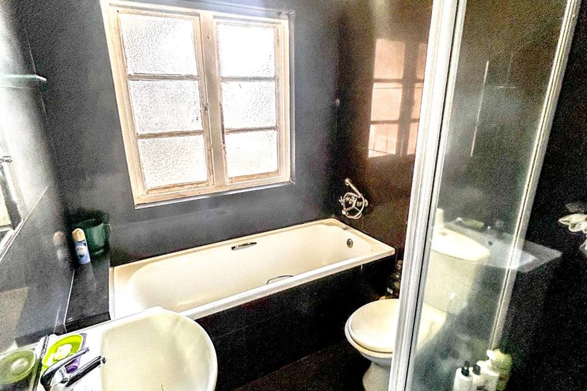 A compact bathroom featuring a bathtub, separate shower enclosure, pedestal basin, and toilet with dark wall tiling.