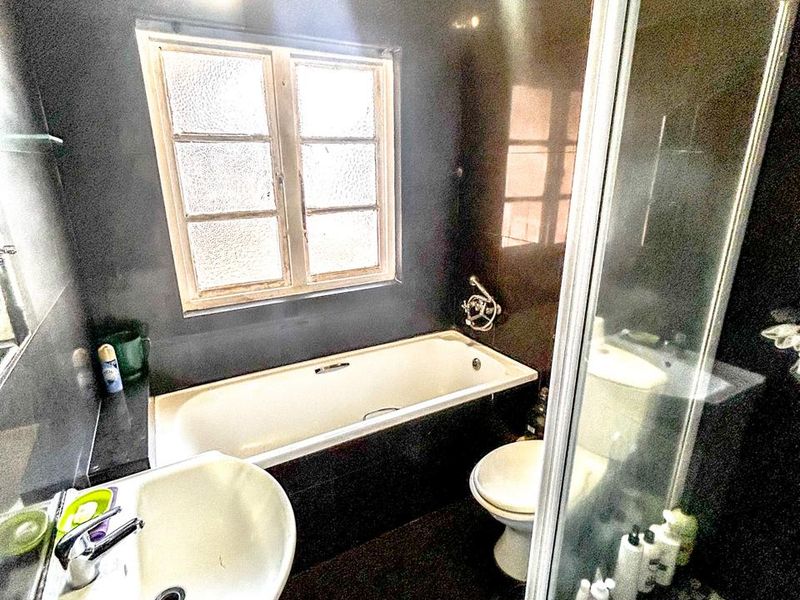 A compact bathroom featuring a bathtub, separate shower enclosure, pedestal basin, and toilet with dark wall tiling.