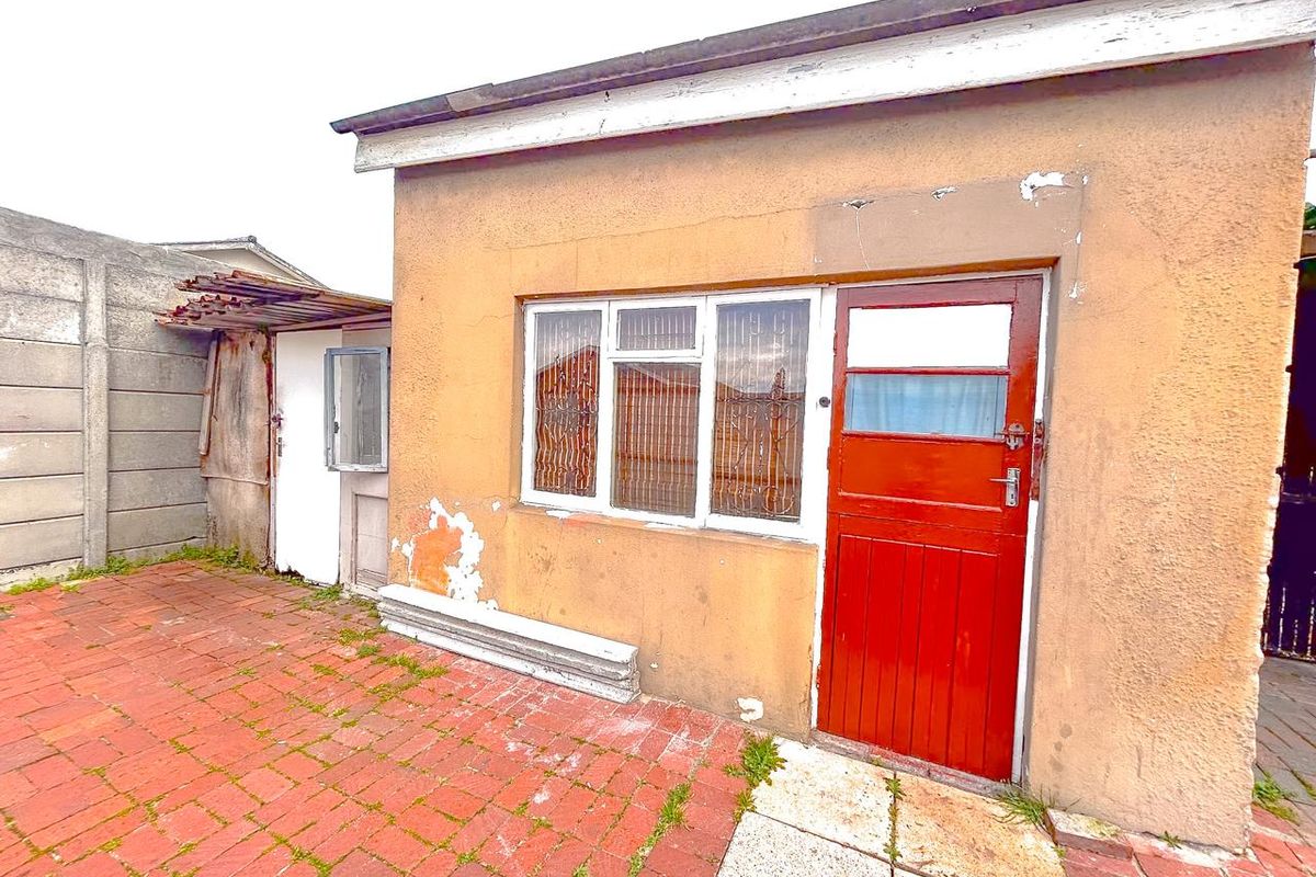 Rear exterior view of the property featuring brick paving, a weathered timber door, and metal window frames with visible signs of exterior wear.