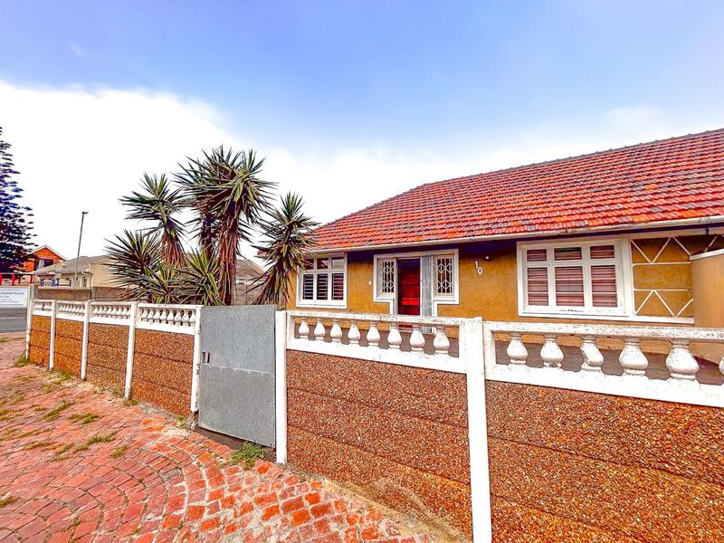 Front elevation of a single-story house featuring a terracotta tiled roof, security-barred windows, and a precast concrete boundary wall with a metal gate.