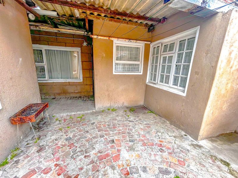 A covered outdoor patio area featuring brick paving and weathered plastered walls, requiring maintenance and potential renovation to improve the exterior living space.