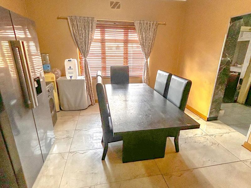 A dining room featuring large format tiled flooring, neutral wall tones, and a window fitted with venetian blinds.