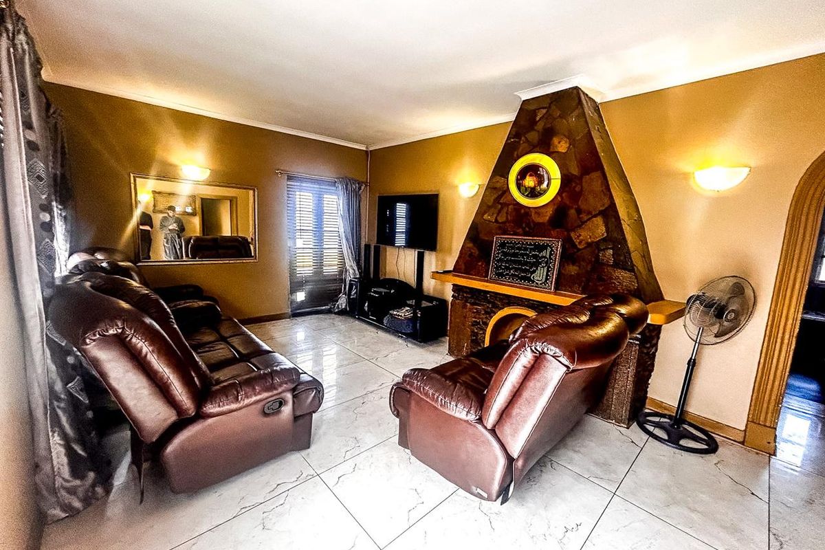 A living room featuring a prominent stone fireplace, large format tiled flooring, and wall-mounted lighting fixtures.