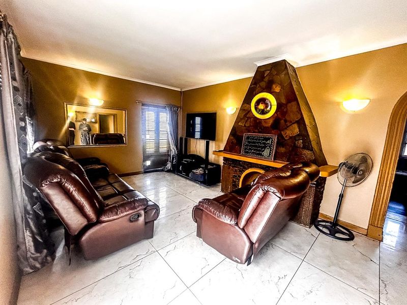 A living room featuring a prominent stone fireplace, large format tiled flooring, and wall-mounted lighting fixtures.