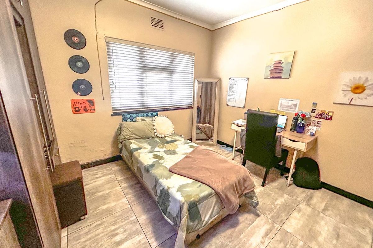 A functional bedroom featuring tiled flooring, a built-in wardrobe, and venetian blinds, offering a practical space with potential for cosmetic updates.