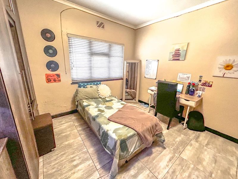 A functional bedroom featuring tiled flooring, a built-in wardrobe, and venetian blinds, offering a practical space with potential for cosmetic updates.