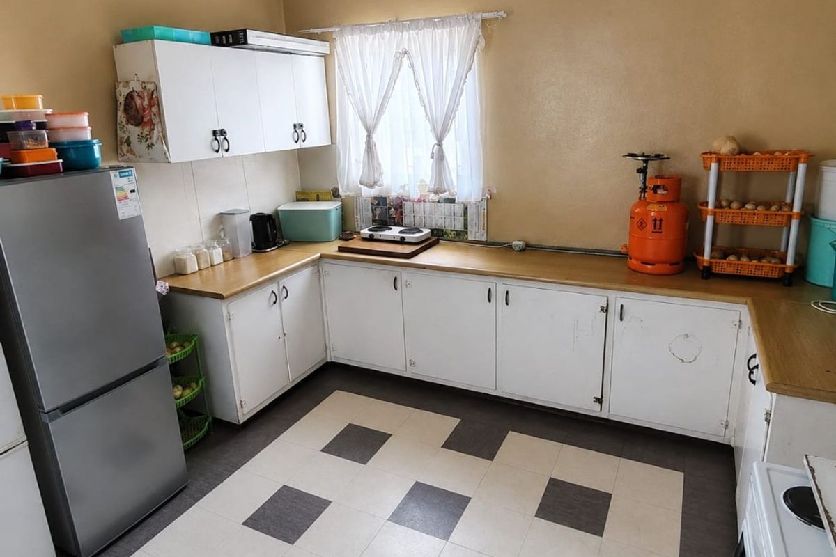 A functional kitchen featuring white cabinetry, laminate countertops, and a checkerboard vinyl floor, offering potential for cosmetic updates.
