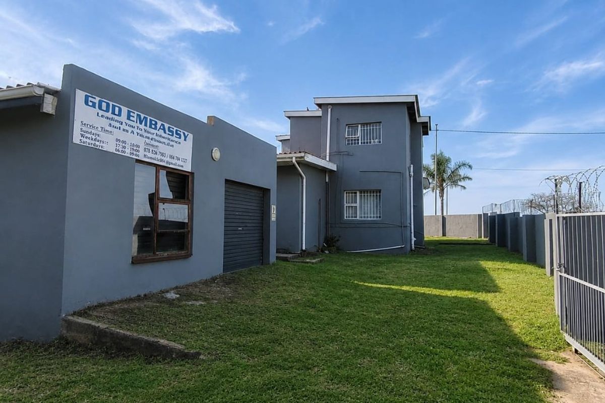 Rear exterior view of the property featuring a lawn, perimeter wall with security fencing, and a detached garage structure.