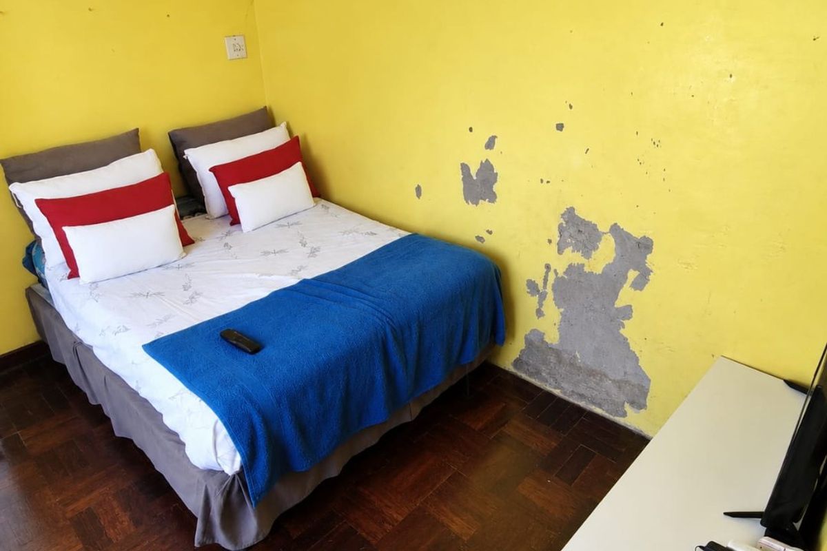 A bedroom featuring dark parquet flooring and yellow walls that require maintenance and repainting due to visible surface damage.