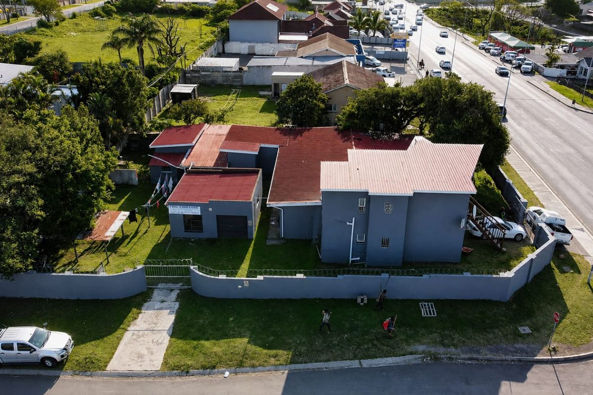 Aerial view of a residential property featuring a multi-section corrugated metal roof, perimeter wall with security fencing, and a driveway.