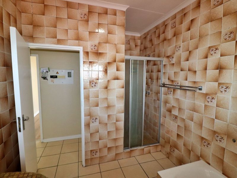 A dated bathroom featuring full-height patterned wall tiles, a shower enclosure, and a tiled floor, presenting an opportunity for modern renovation.