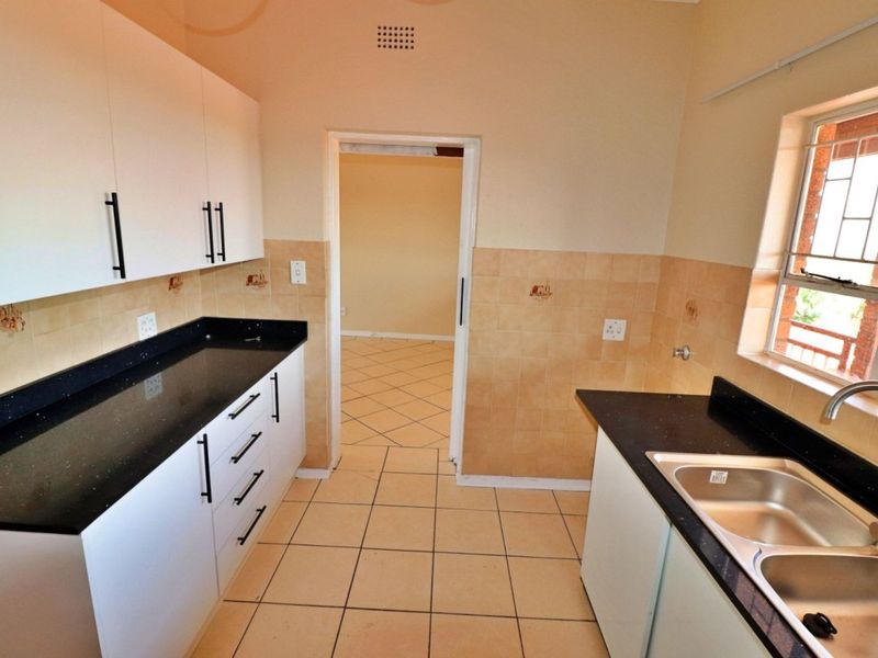 A functional kitchen featuring white cabinetry, dark granite countertops, double stainless steel sink, and neutral ceramic tiling throughout.