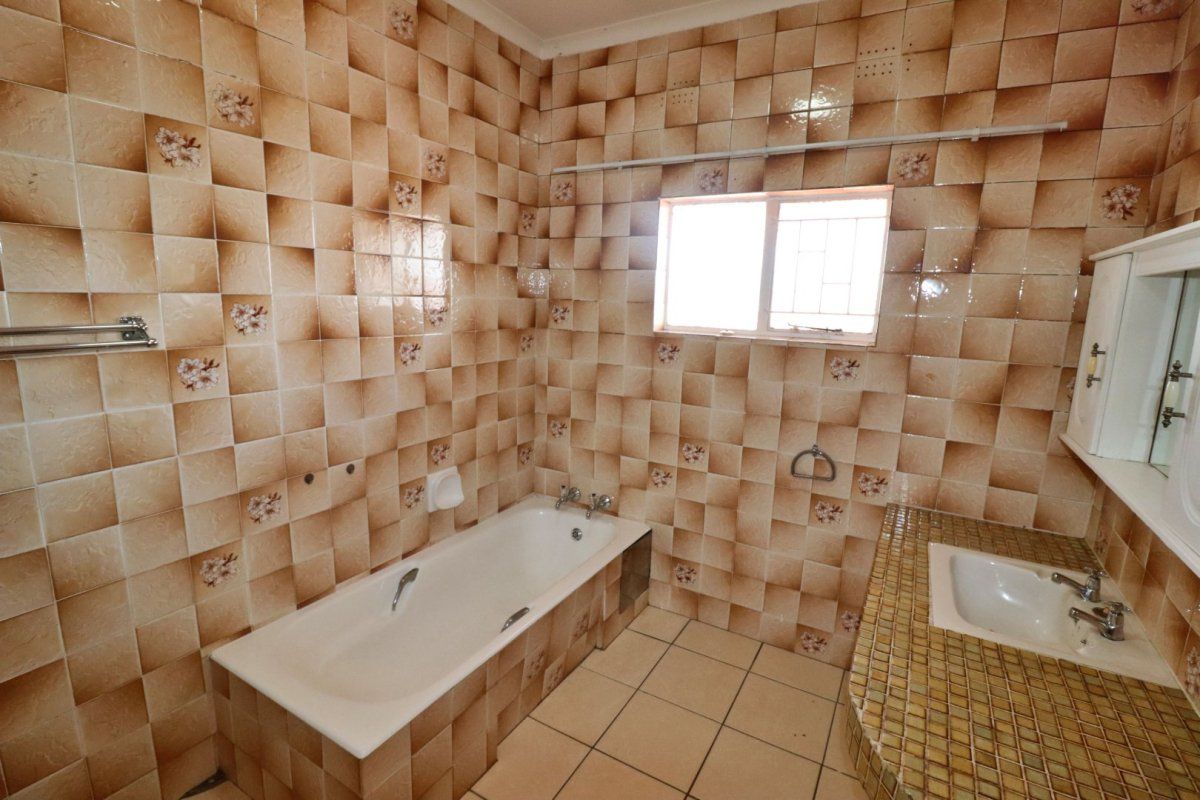 A dated bathroom featuring a built-in bathtub, tiled vanity with integrated sink, and full-height wall tiling.