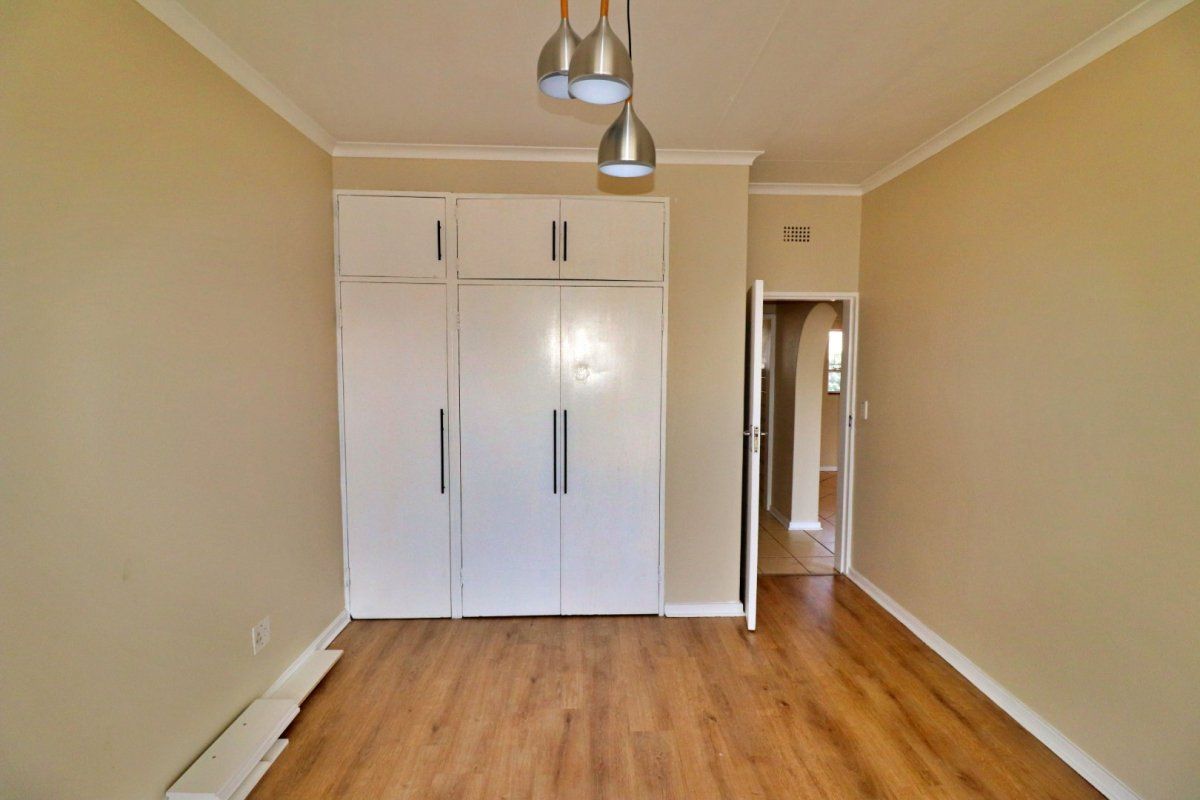 A bright, empty bedroom featuring laminate flooring, built-in cupboards with overhead storage, and modern pendant lighting.