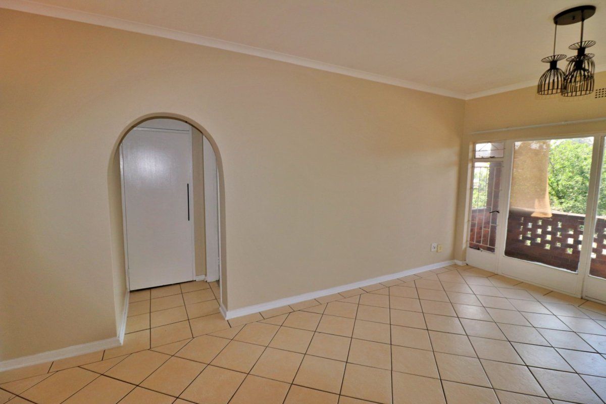 An empty living room featuring neutral tiled flooring, an arched entryway, and a sliding glass door providing access to an outdoor balcony area.