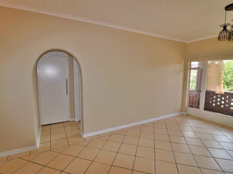 An empty living room featuring neutral tiled flooring, an arched entryway, and a sliding glass door providing access to an outdoor balcony area.