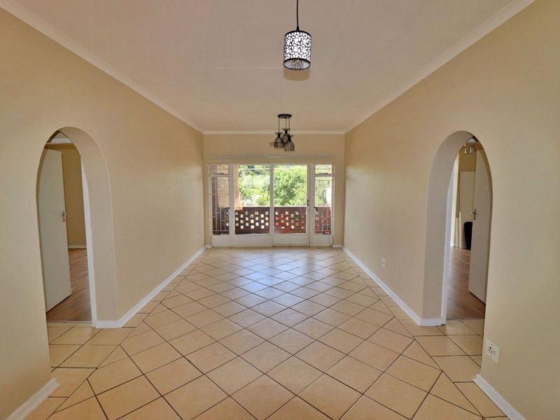 Spacious, empty living area featuring neutral tiled flooring, distinctive archway entrances, and a sliding glass door leading to an outdoor balcony.
