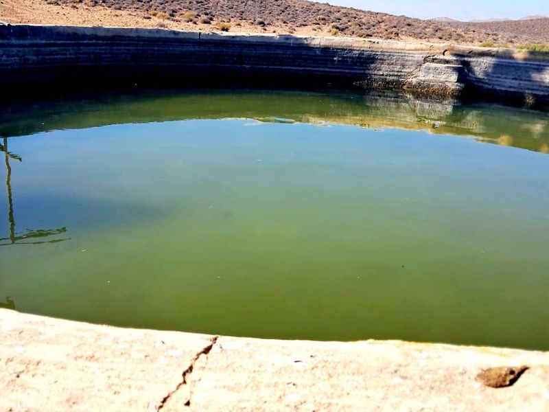 A large circular concrete farm reservoir used for water storage, set within a rural landscape.