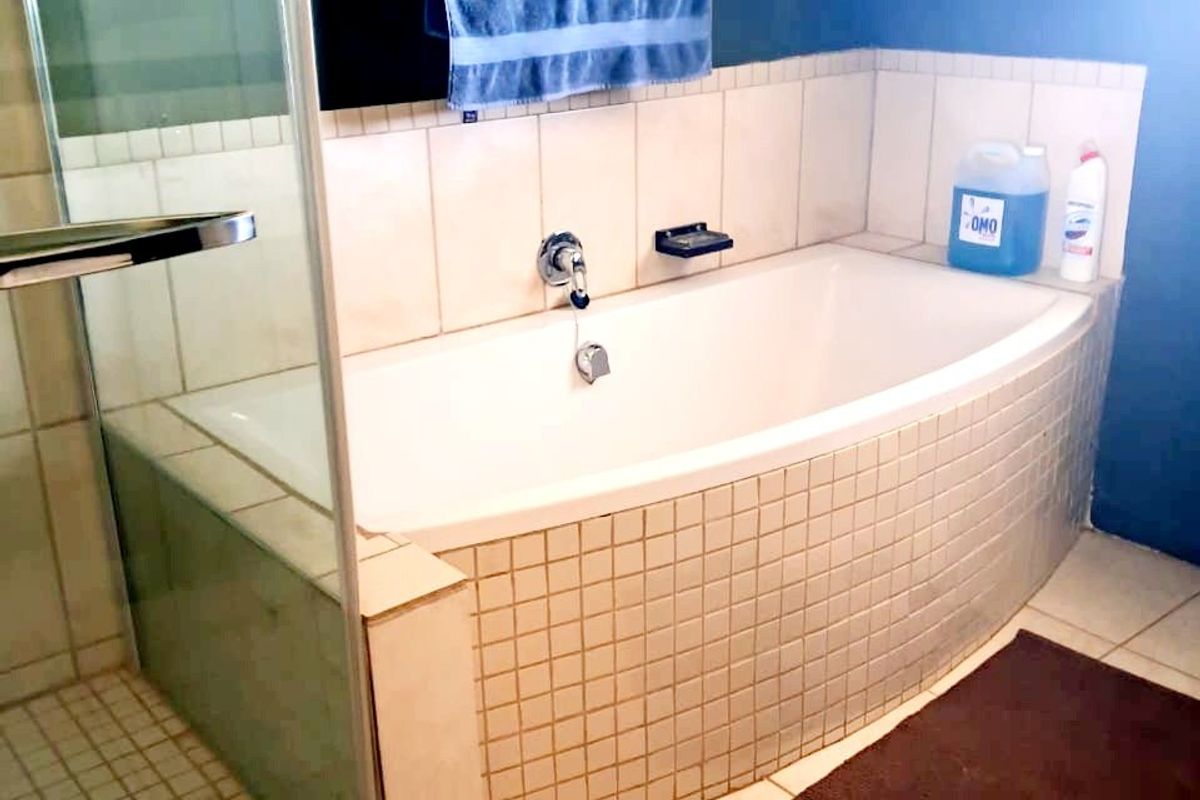 A functional bathroom featuring a built-in bathtub with tiled surround and a separate glass-enclosed shower area with neutral floor tiling.