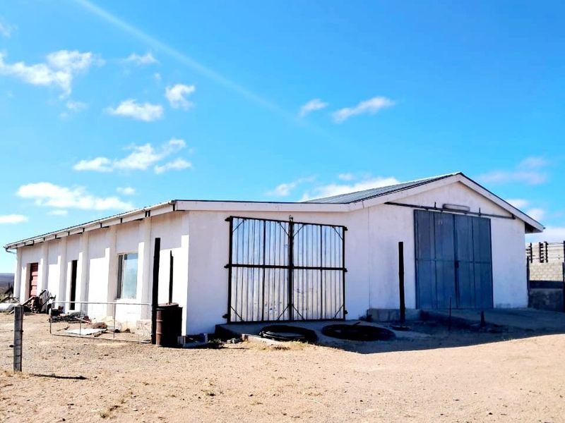 A functional farm outbuilding featuring large metal sliding doors, security gates, and a durable corrugated roof, situated on a clear, open plot.