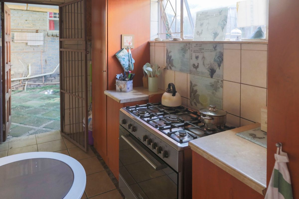 A functional kitchen featuring a gas stove, built-in cabinetry, and tiled splashbacks, with direct access to an outdoor paved area.