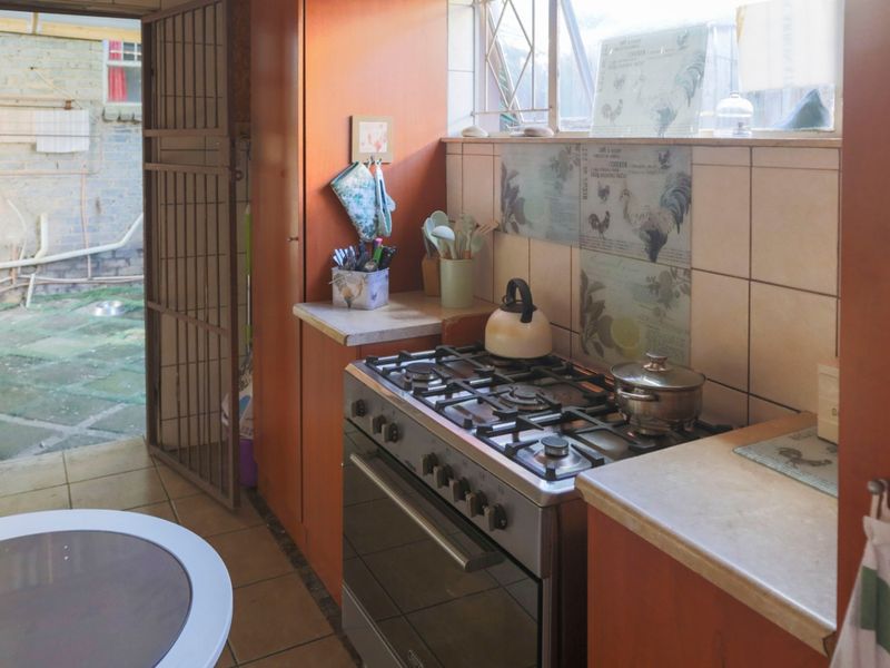 A functional kitchen featuring a gas stove, built-in cabinetry, and tiled splashbacks, with direct access to an outdoor paved area.