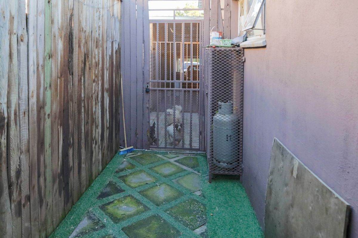 A narrow side passage featuring a security gate, timber fencing, and paved walkway with some signs of weathering and maintenance required.