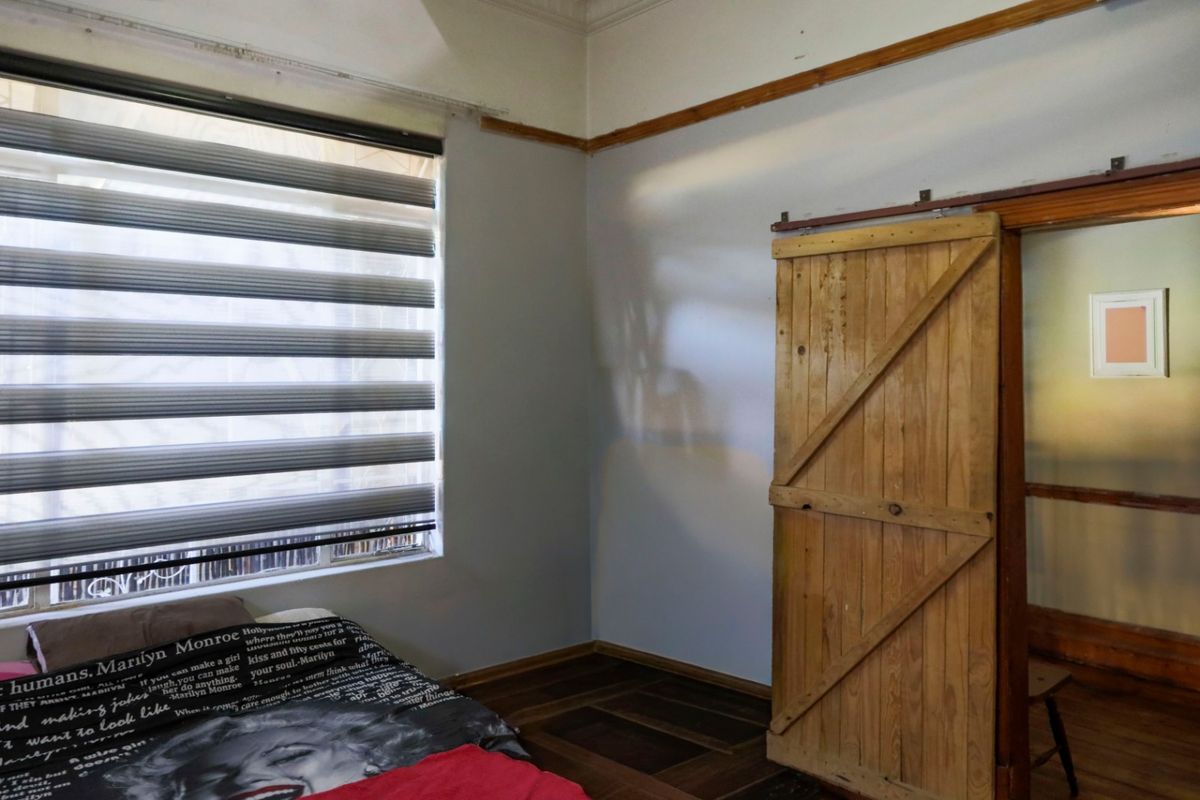 Bedroom featuring wooden parquet flooring, a rustic sliding barn door, and modern zebra blinds, offering a blend of classic and contemporary elements.