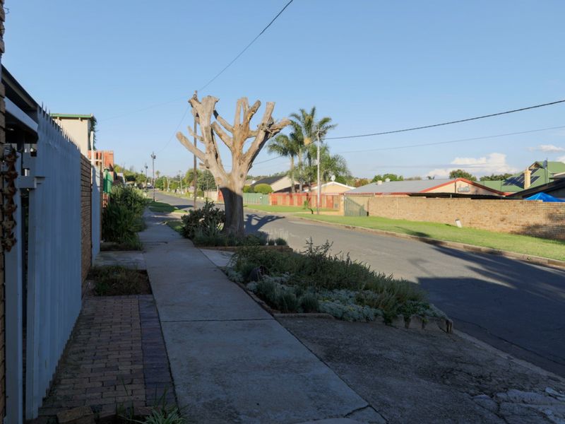 A view of the residential street showing the sidewalk, boundary wall, and surrounding neighborhood landscape.
