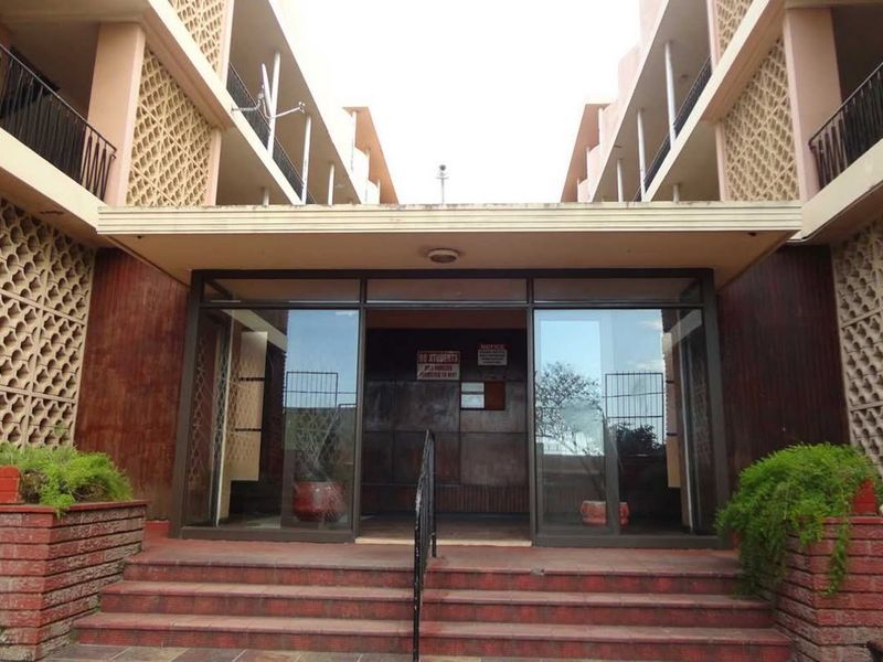 The front entrance of the apartment building features a brick staircase, decorative breeze block walls, and glass sliding doors leading into the lobby.