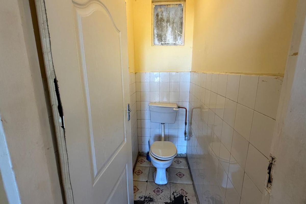 A small, dated bathroom featuring a standard toilet, tiled walls, and floor. The space requires renovation and cosmetic updates to improve its condition.