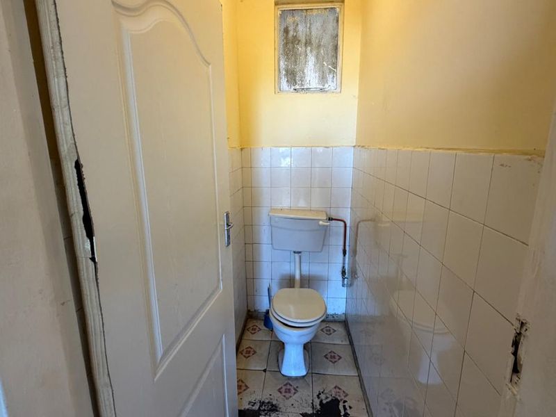 A small, dated bathroom featuring a standard toilet, tiled walls, and floor. The space requires renovation and cosmetic updates to improve its condition.