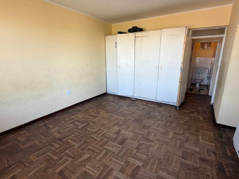 A bedroom featuring parquet flooring and a built-in wardrobe, with an adjacent bathroom visible through the doorway.