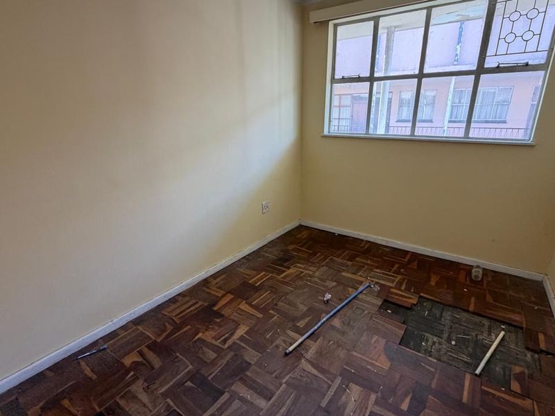 An empty bedroom featuring original parquet flooring that requires repair, complemented by a large multi-pane window providing natural light.