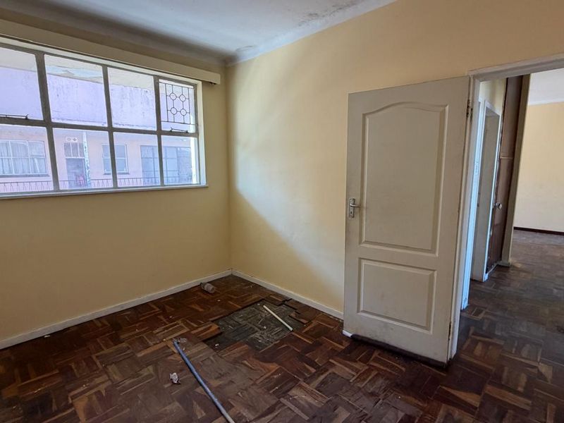 An empty bedroom featuring original parquet flooring in need of repair and a steel-framed window, offering a blank canvas for renovation.