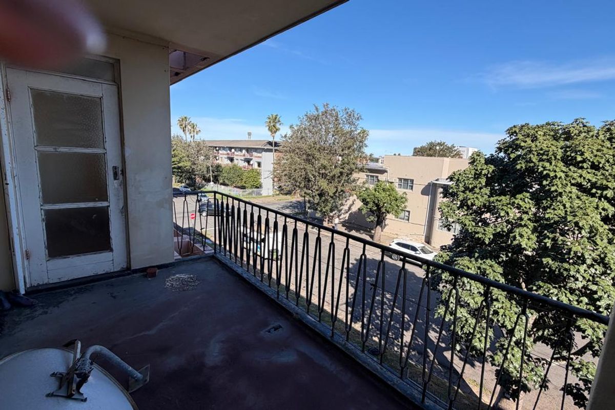 An open balcony featuring a wrought iron railing and concrete flooring, offering an elevated view of the surrounding neighborhood.