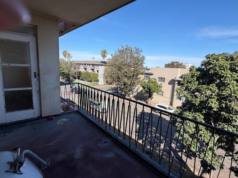 An open balcony featuring a wrought iron railing and concrete flooring, offering an elevated view of the surrounding neighborhood.