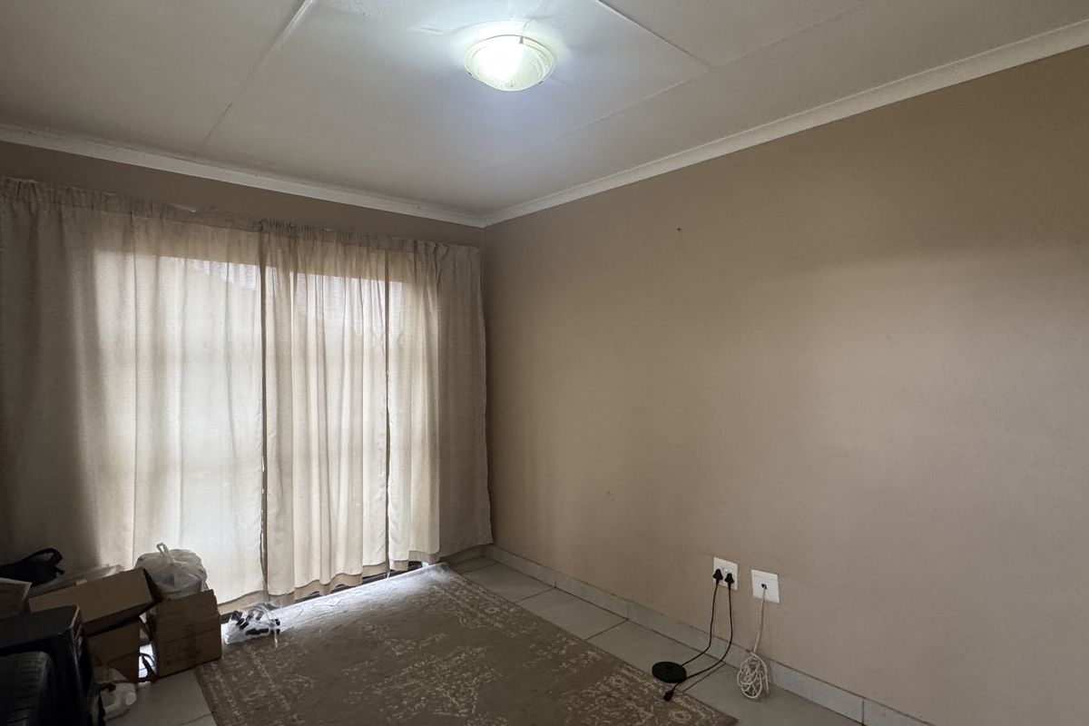 A vacant living room featuring tiled flooring, a sliding glass door providing natural light, and neutral wall finishes.