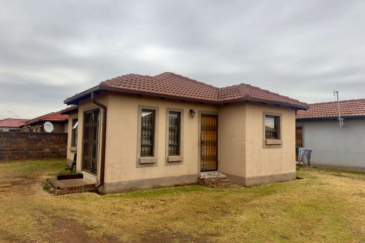 A detached single-story house featuring a tiled roof, security gates, and exterior wall lighting, set within a modest garden area.