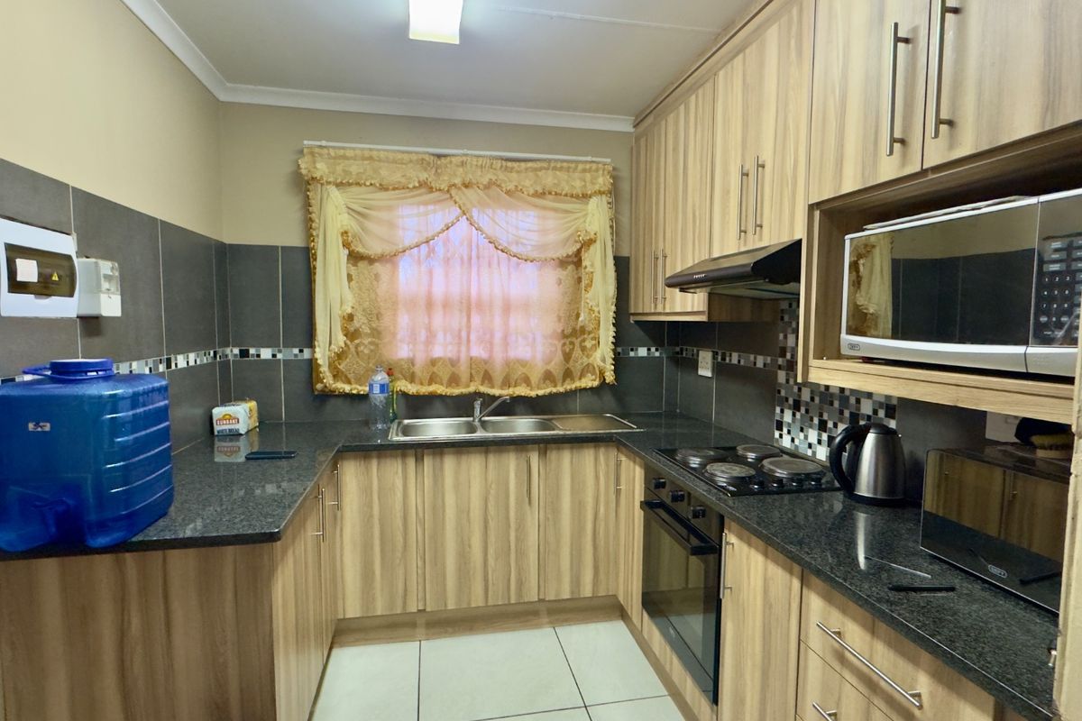 A functional kitchen featuring wood-look cabinetry, granite countertops, a double basin sink, and built-in electric cooking appliances with tiled finishes.