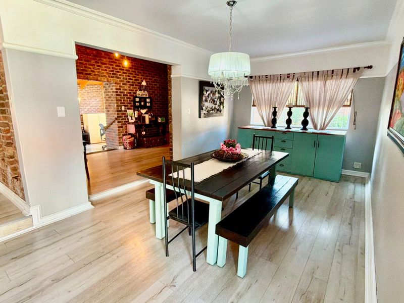 A bright dining room featuring laminate flooring, crown molding, and an exposed brick accent wall, with built-in cabinetry and a central pendant light fixture.
