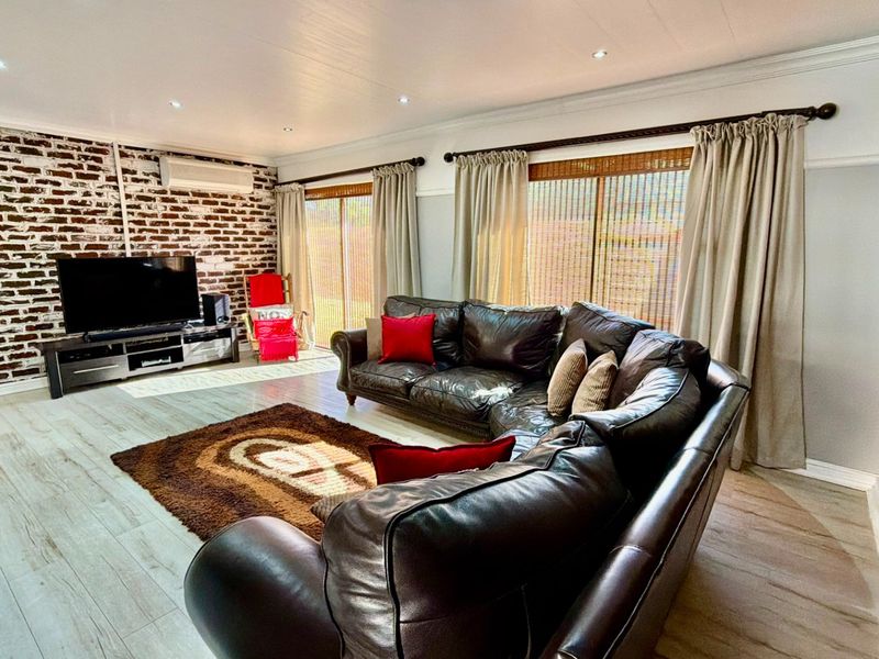 Spacious living room featuring an exposed brick accent wall, wood-look flooring, recessed lighting, and sliding glass doors providing access to the exterior.